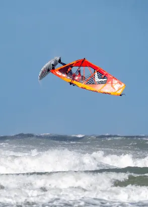 Windsurfer met oranje zeil in een loop boven de golf