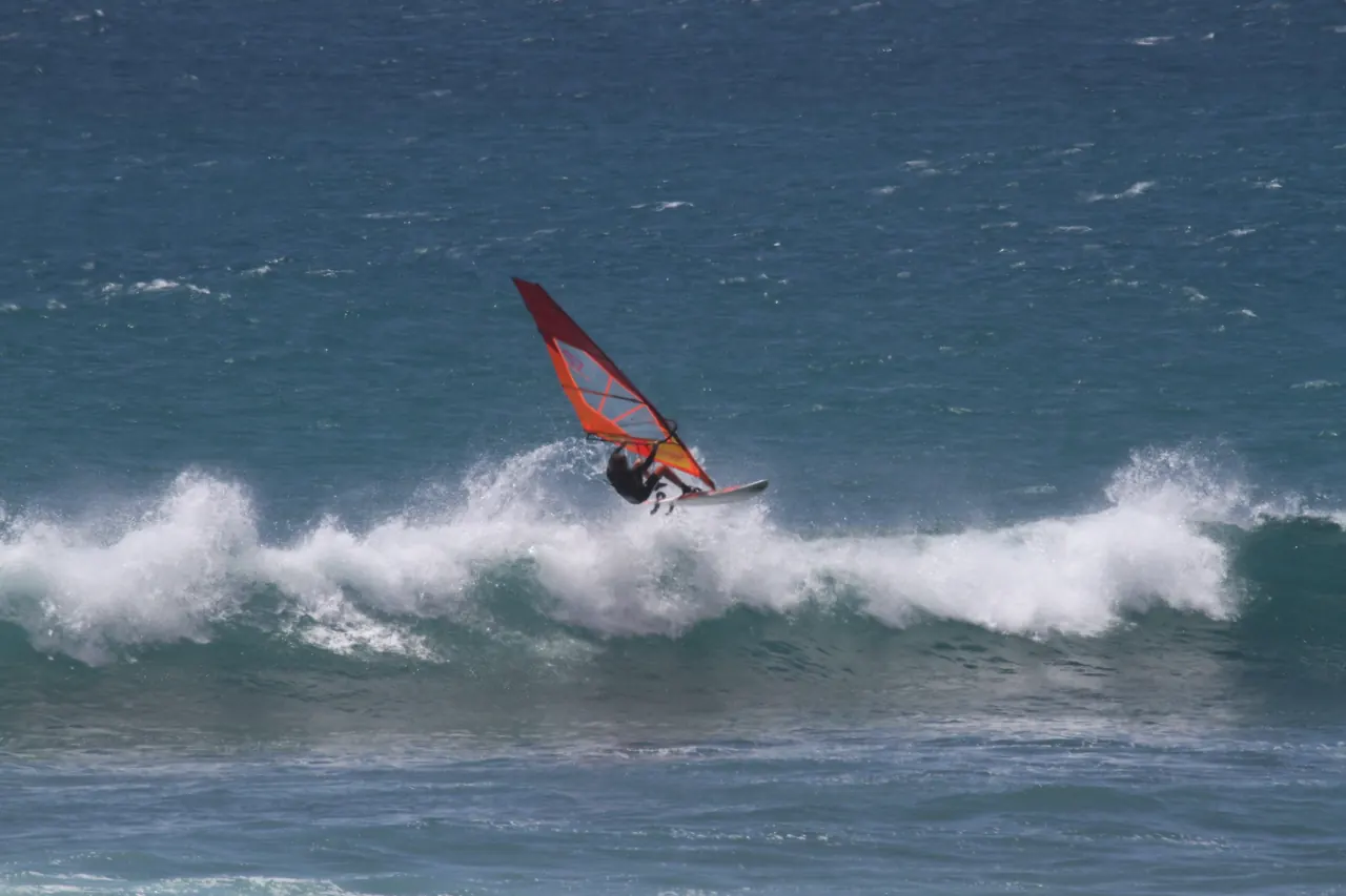 Windsurfer met rood zeil voor de witte golf
