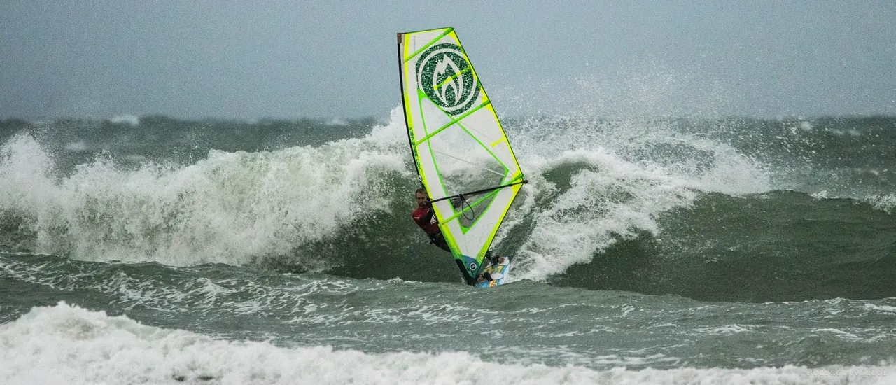 Windsurfer met geel zeil op een brekende golf