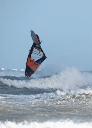 Windsurfer met zwart-rood zeil boven het schuim