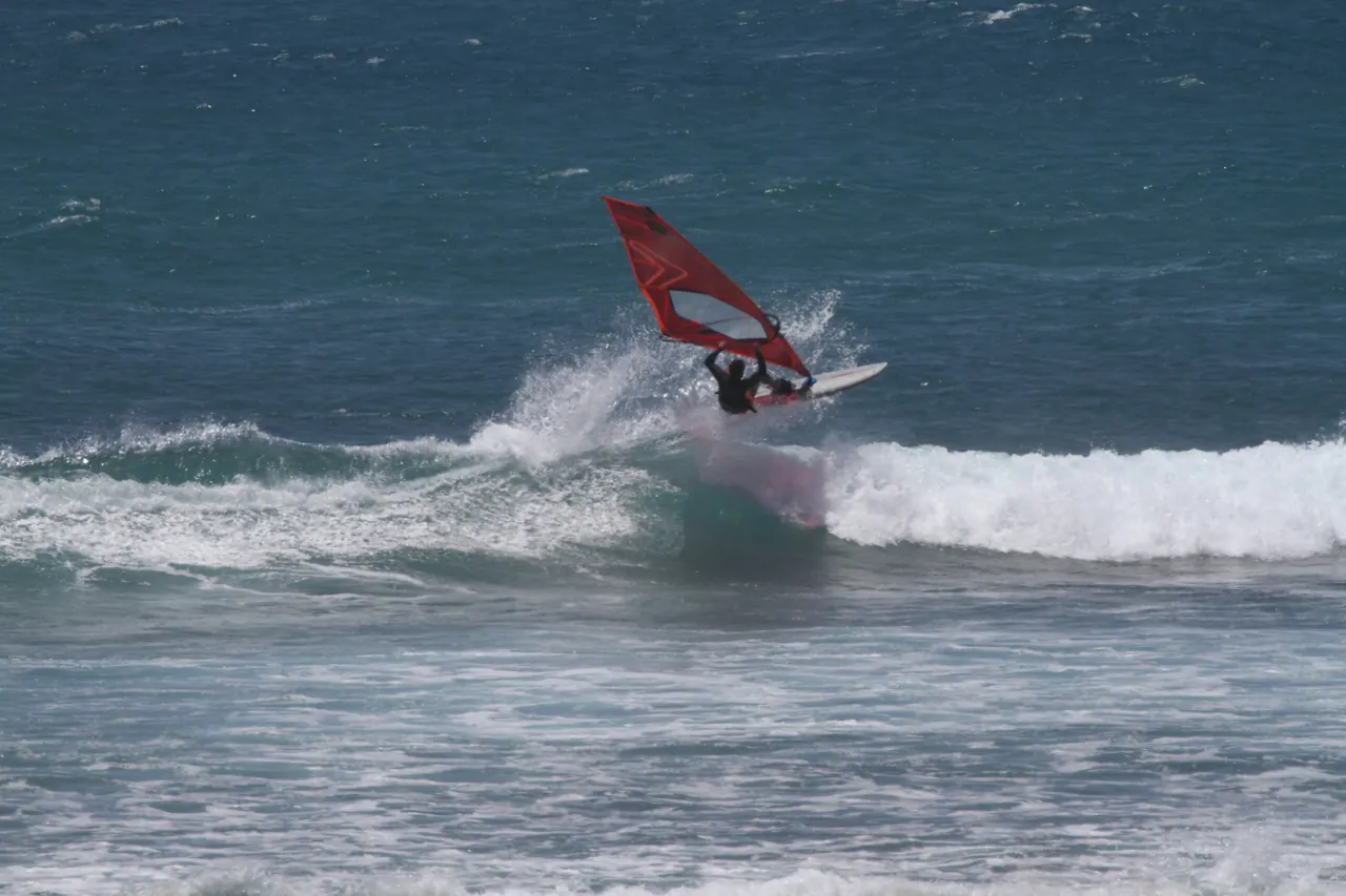 Windsurfer met rood zeil op een brekende golf