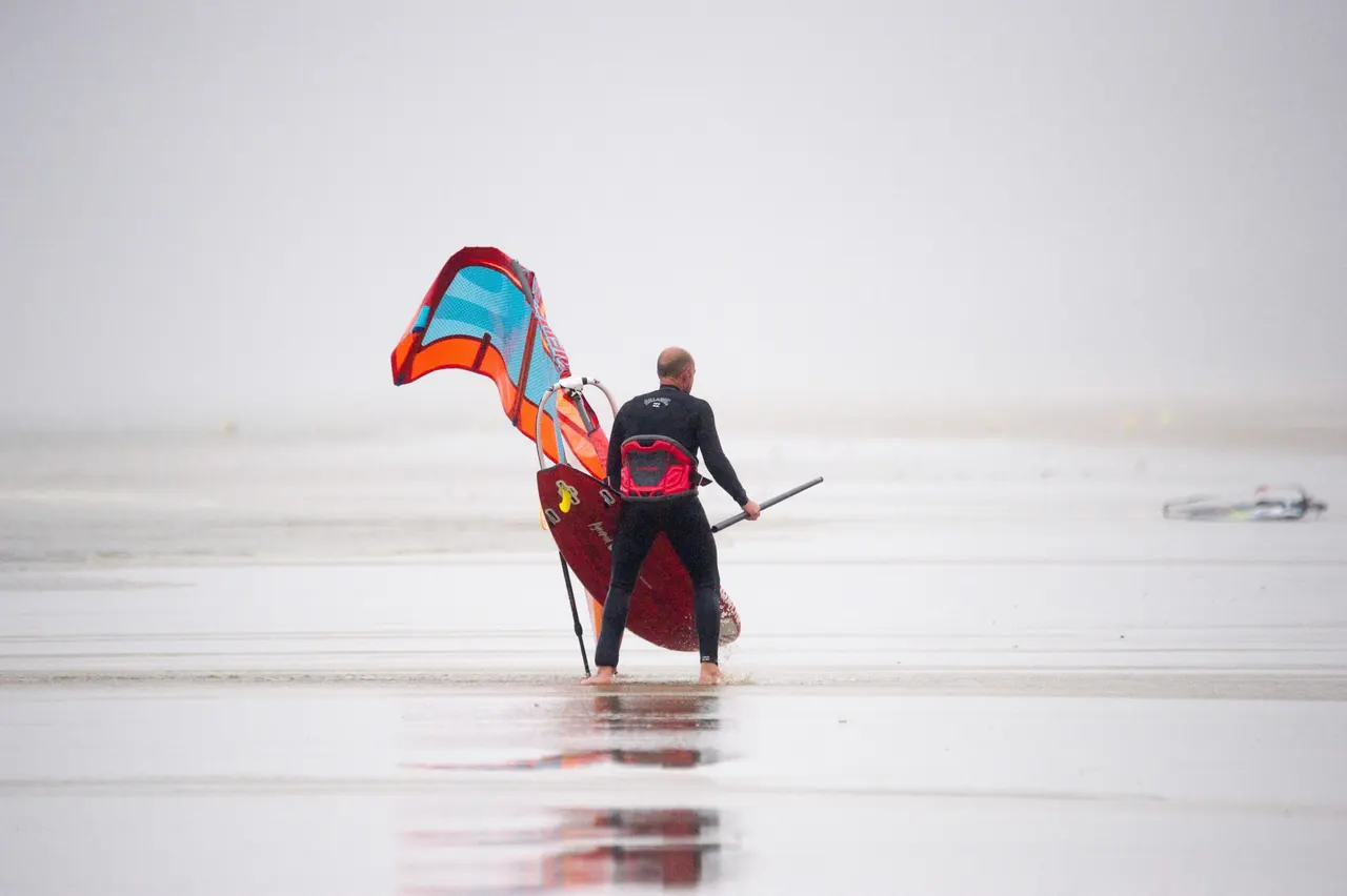 Windsurfer draagt zijn zeil over het natte strand