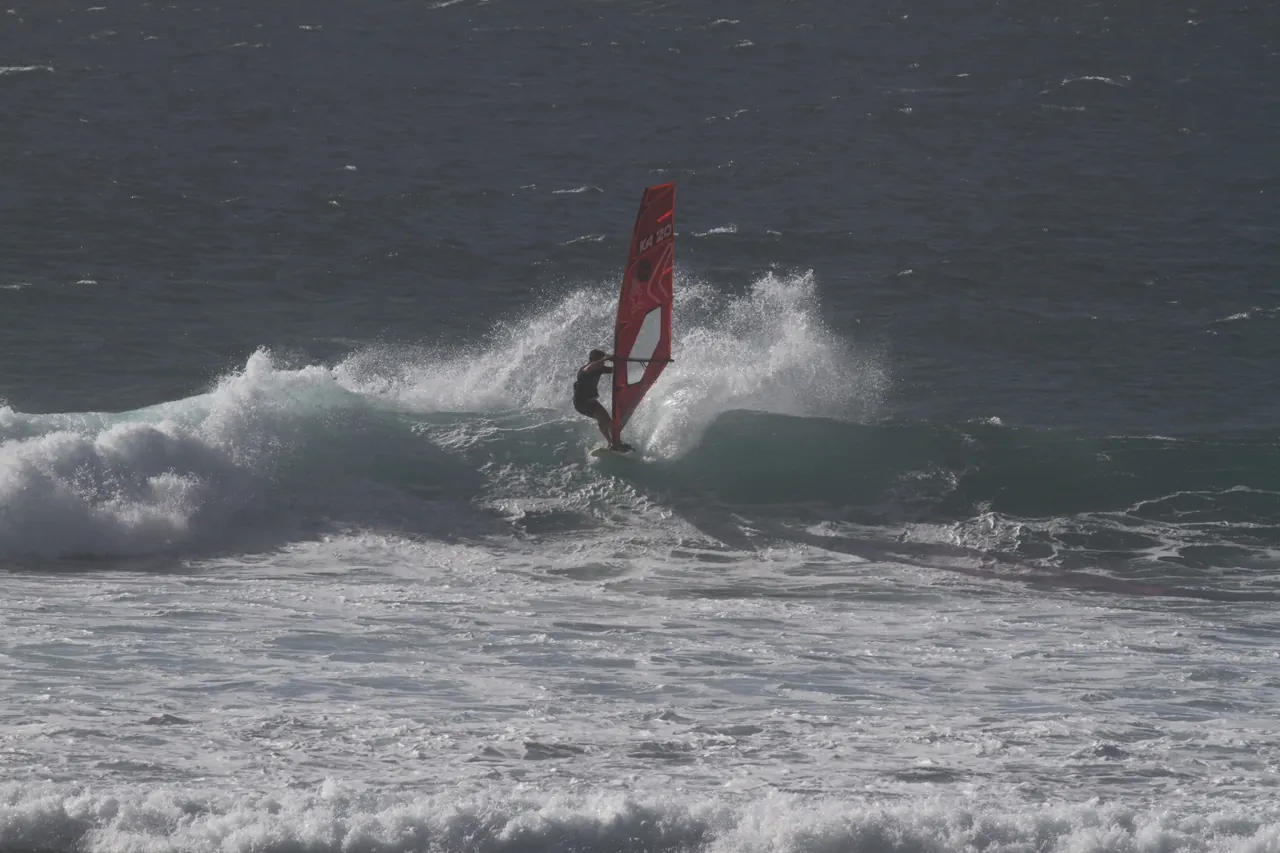 Windsurfer met rood zeil op een brekende golf
