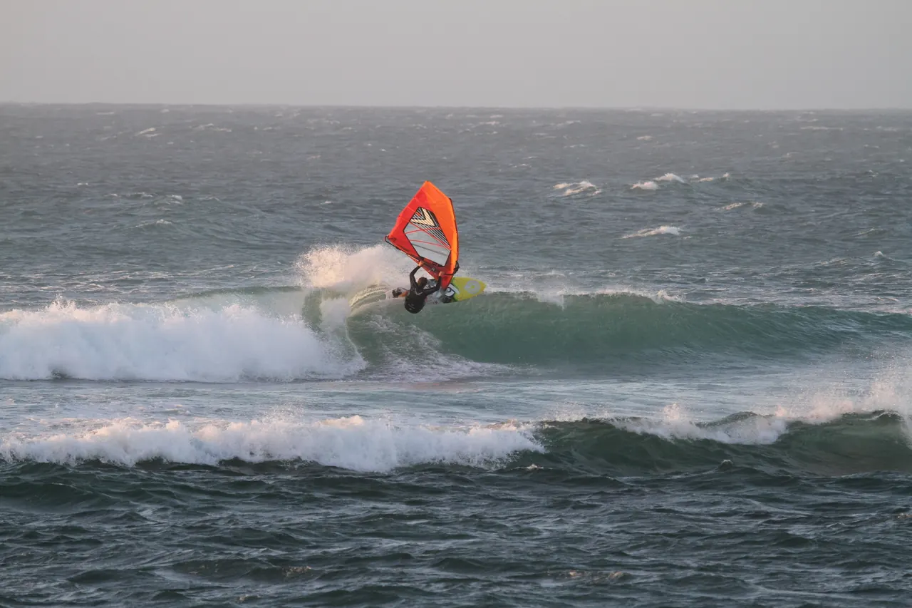 Windsurfer met oranje zeil op een golf