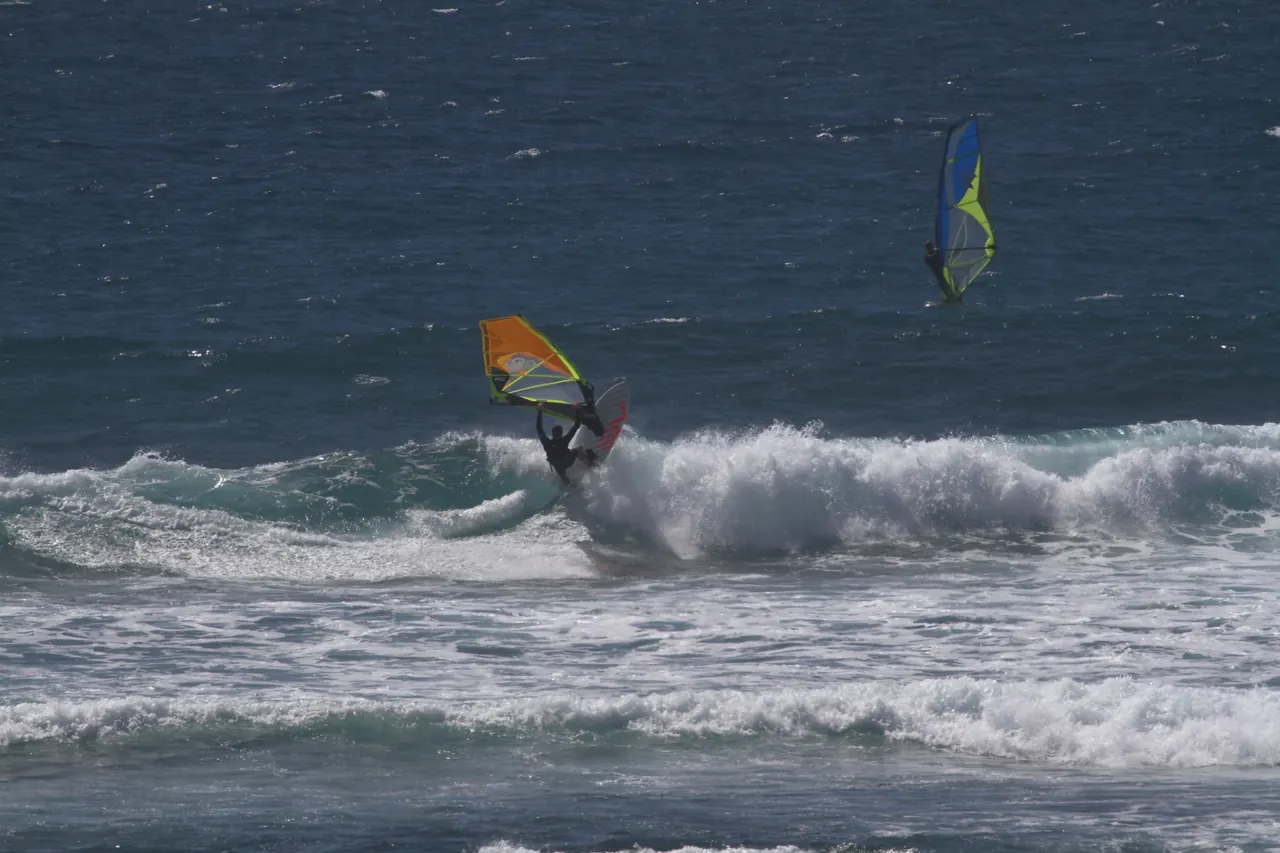 Twee windsurfers op dezelfde golf