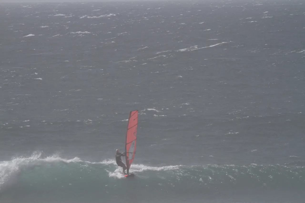 Windsurfer met rood zeil op een golf