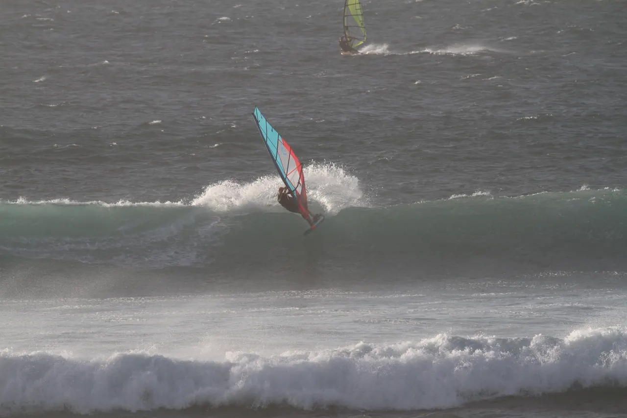 Windsurfer met blauw zeil op een golf