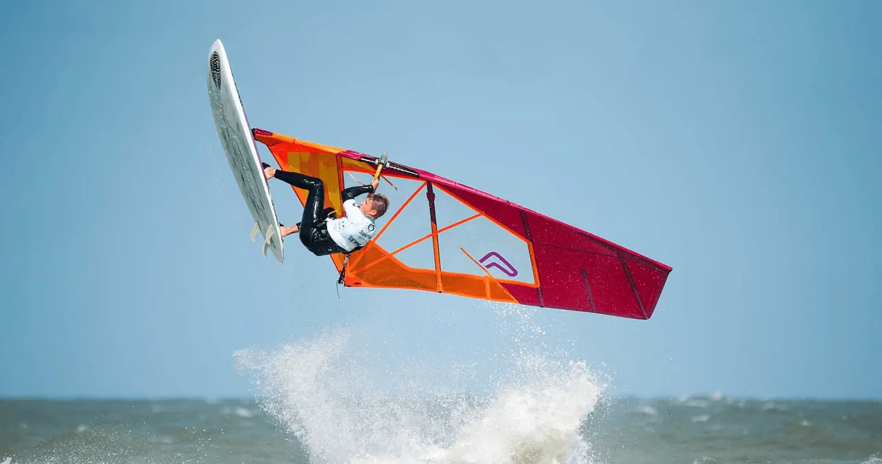 Windsurfer met oranje-rood zeil in de lucht