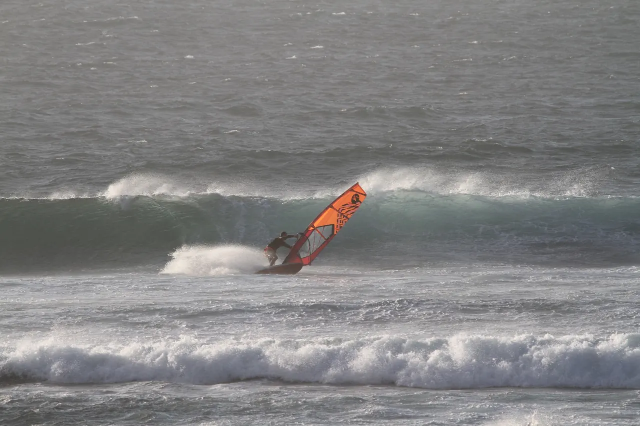 Windsurfer met oranje zeil op een golf