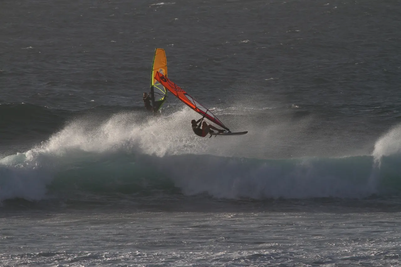 Windsurfer met oranje zeil in de lucht boven de golf