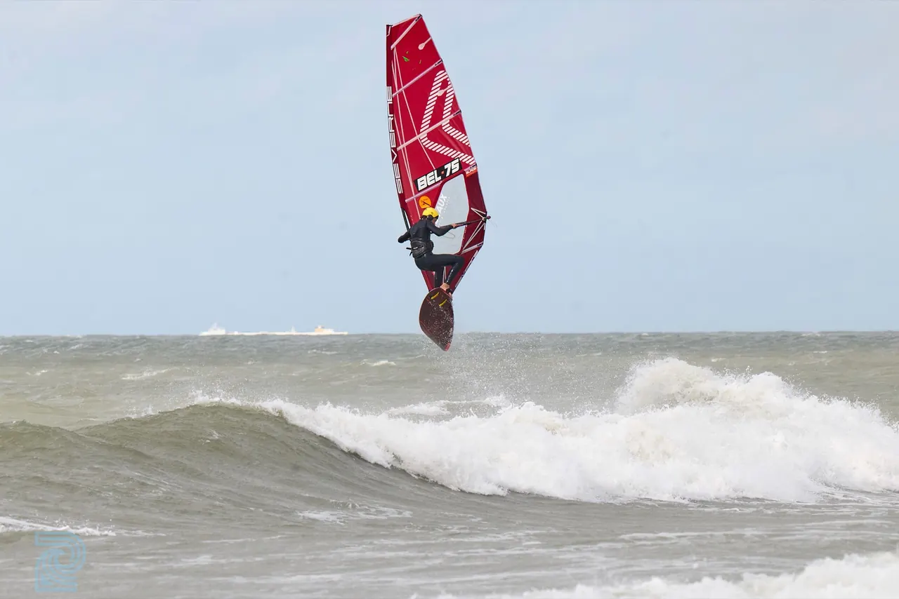 Jonge windsurfer in een rood zeil boven een golf