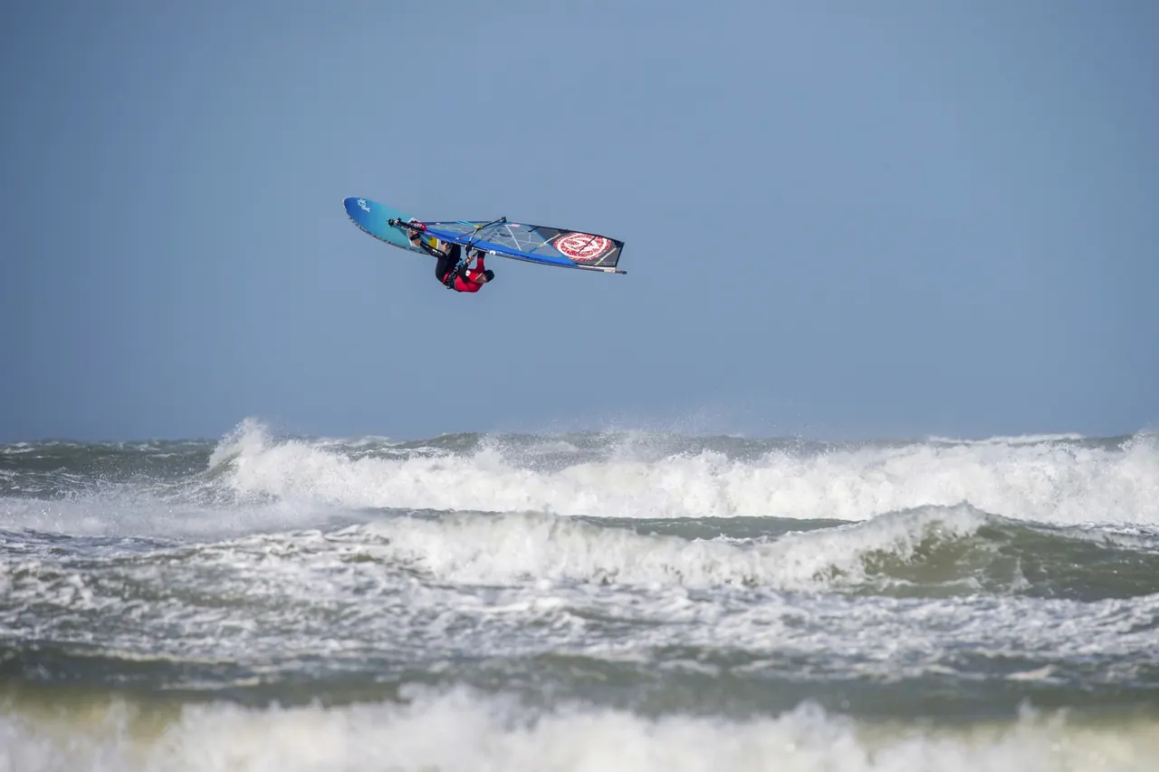 Windsurfer hoog in de lucht met blauw zeil